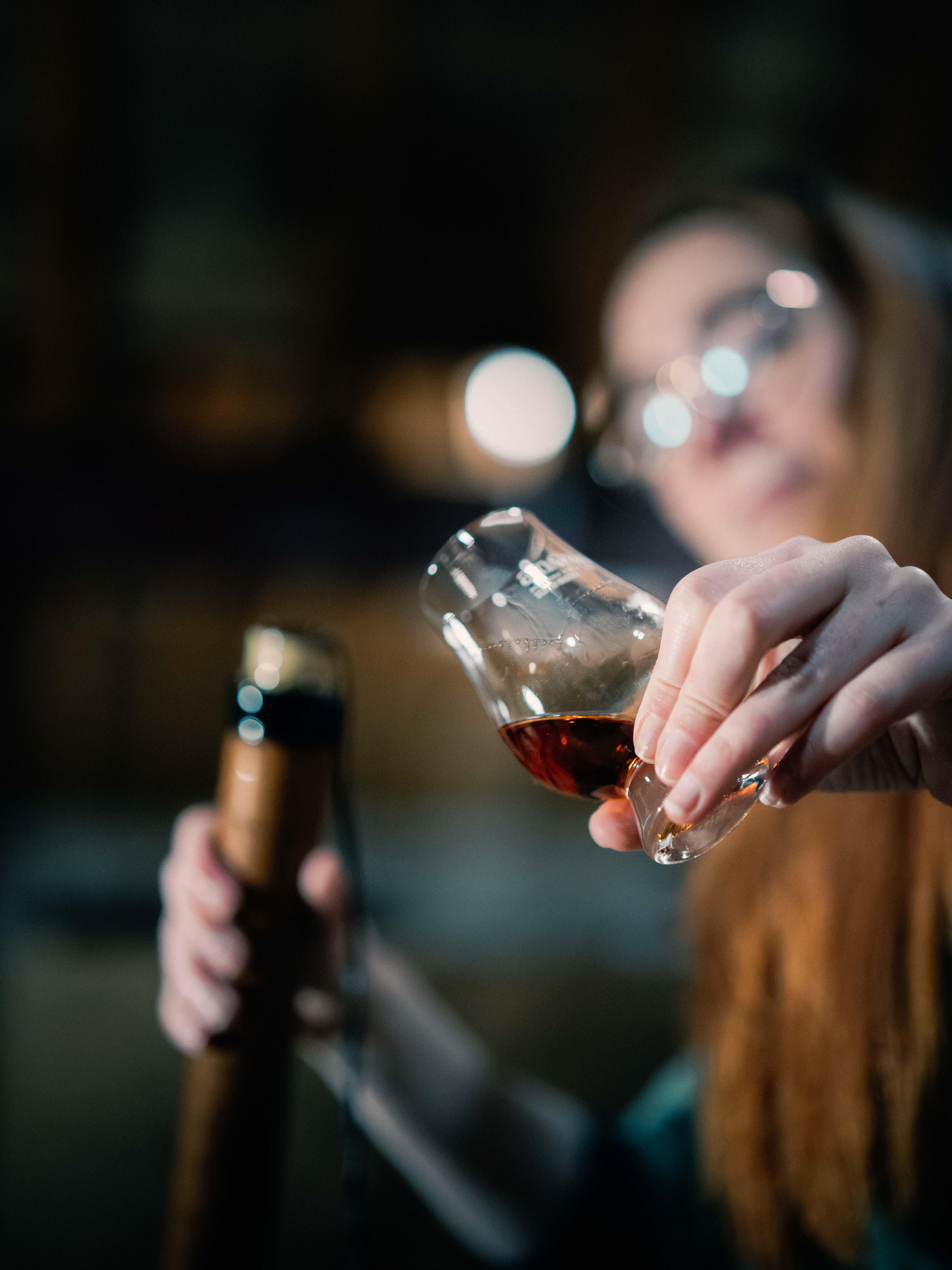 A woman holds up a small glass of whisky to the camera